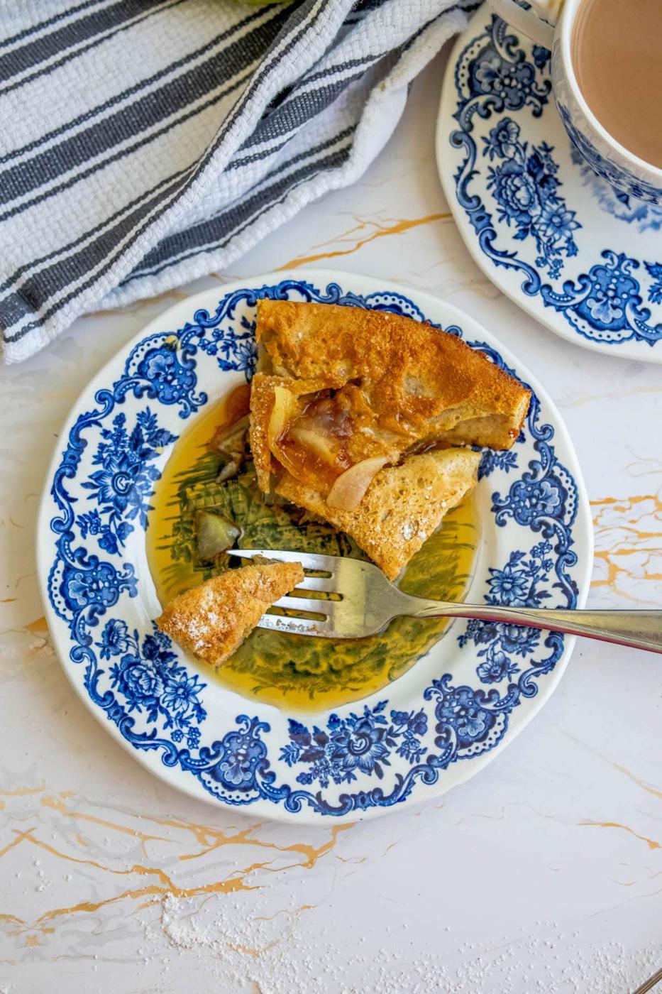 A blue and white plate with a slice of bread and a cup of tea, alongside a cinnamon apple dutch baby.