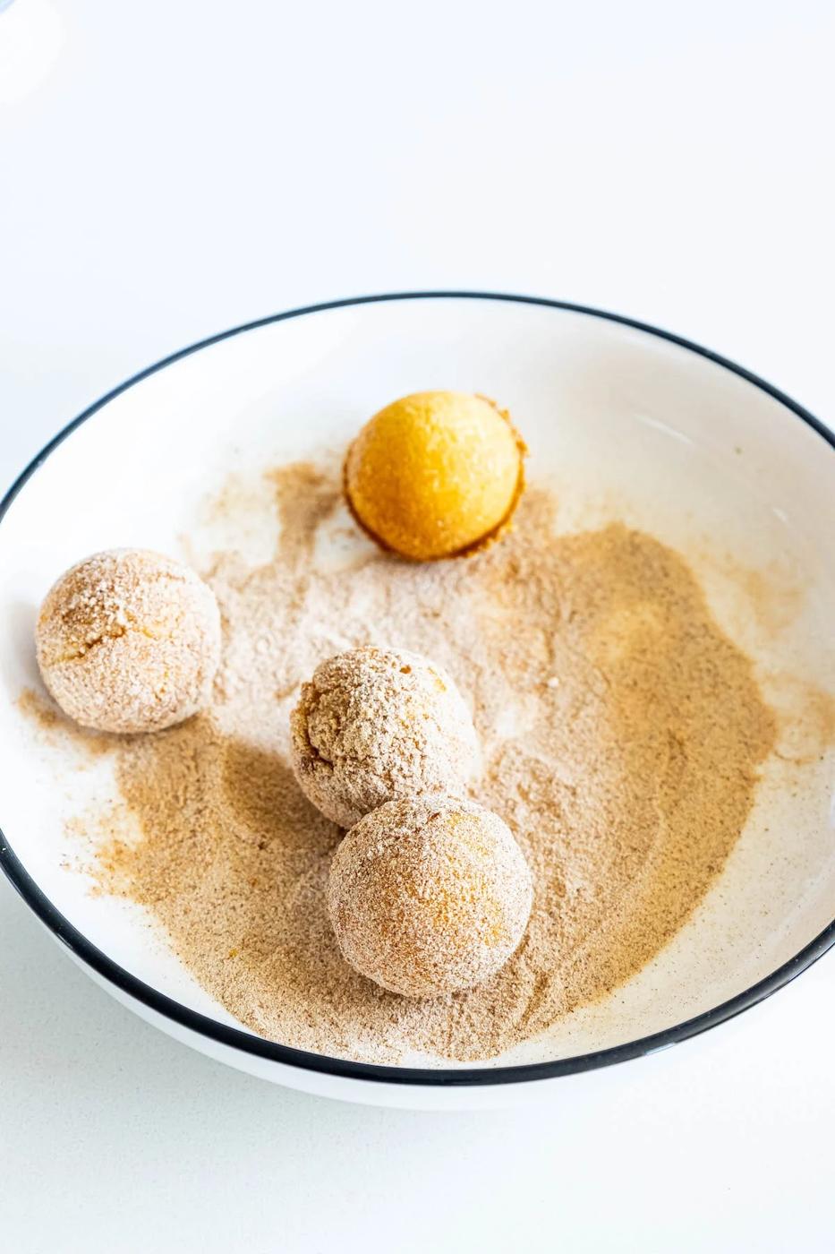 picture of donut holes being rolled in a bowl of cinnamon sugar