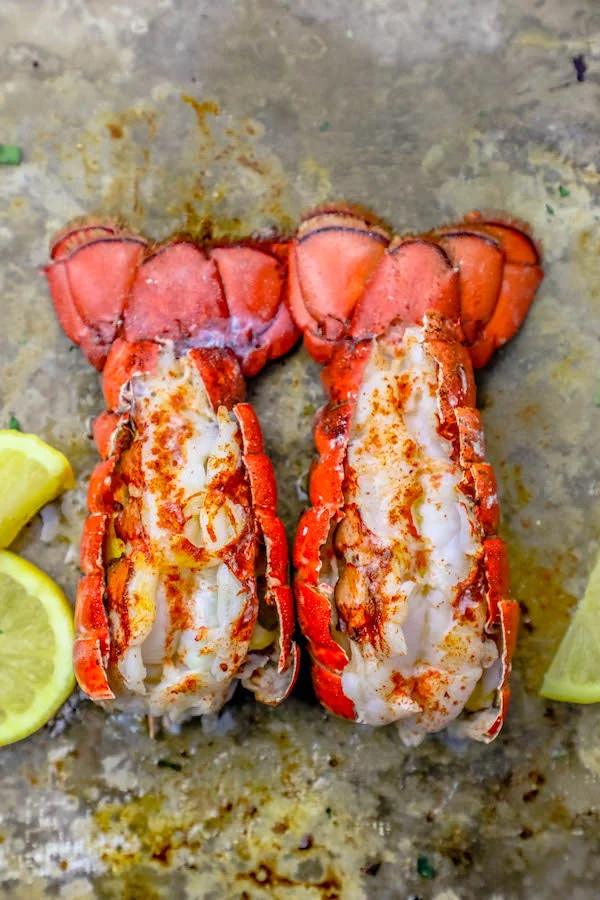 Two broiled lobster tails on a baking sheet with lemon wedges, showcasing the best lobster tail recipe.