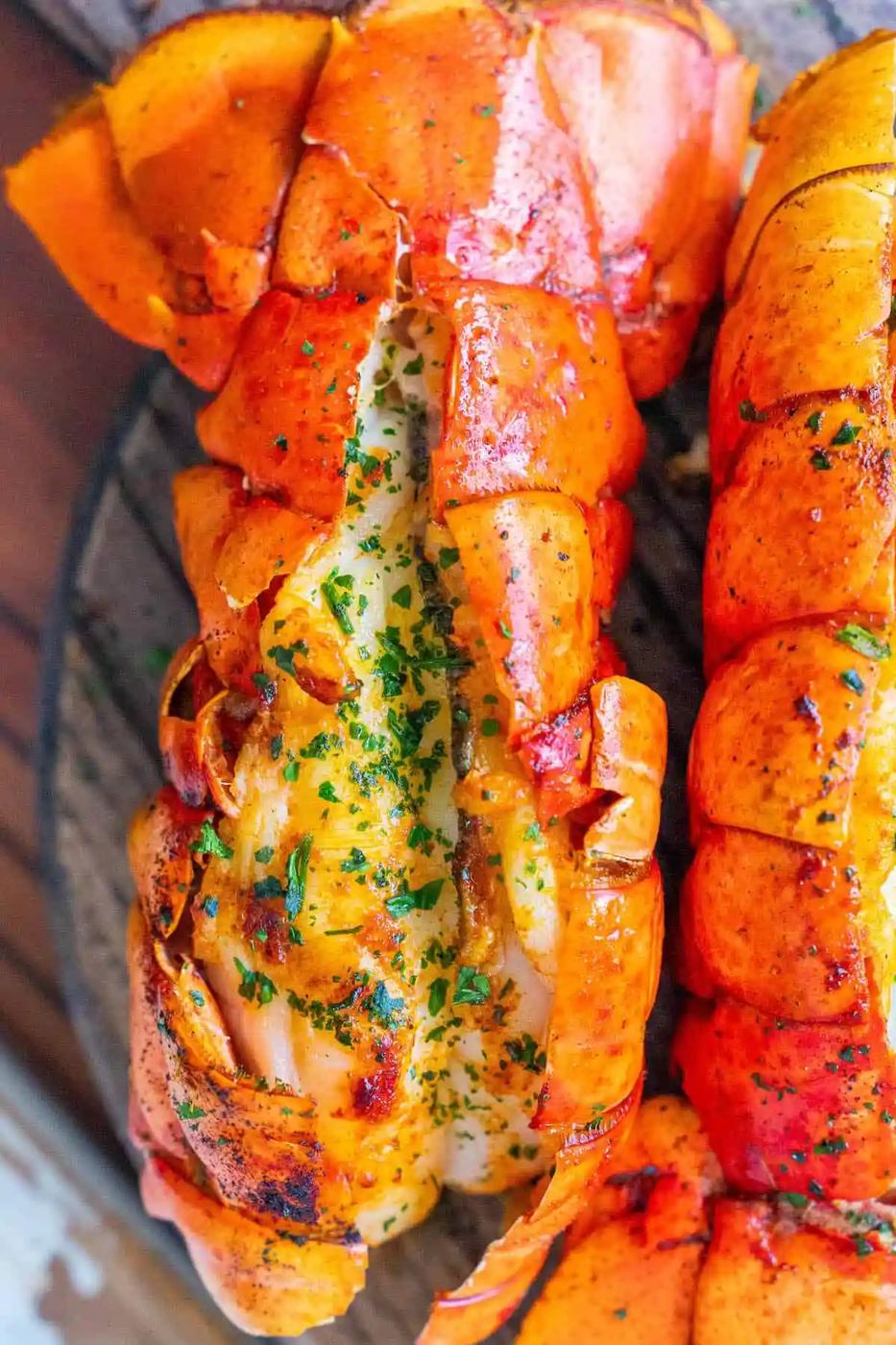 The Best Easy Broiled Lobster Tails Ever - Two lobster tails on a wooden plate.