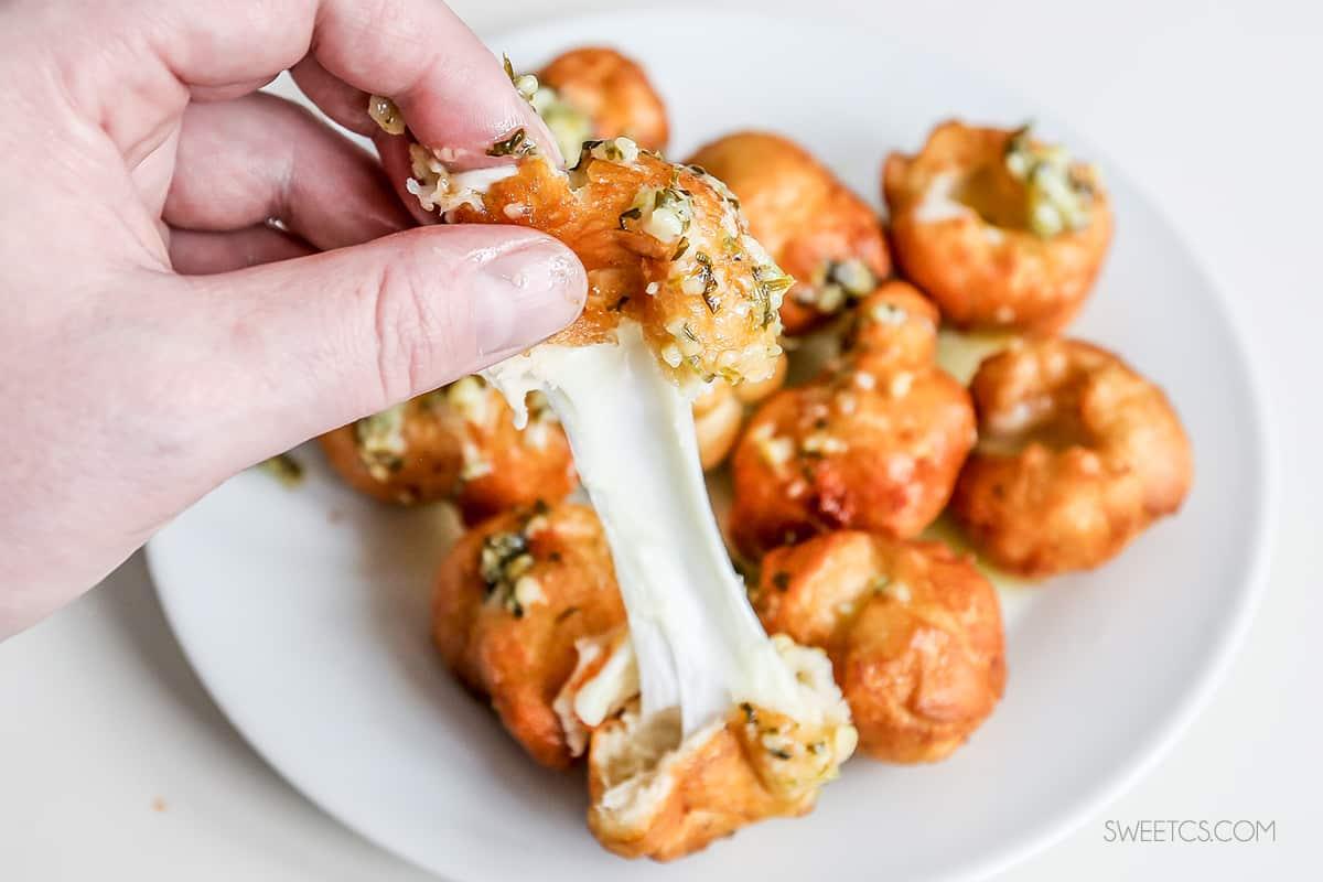 A person enjoying fried cheese bombs by dipping a fork into a plate of crispy delights.