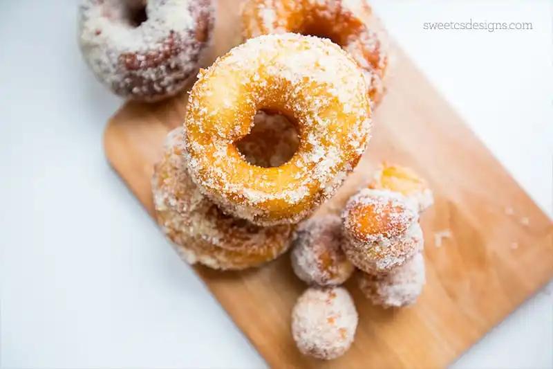 Sugared donuts on a wooden cutting board.