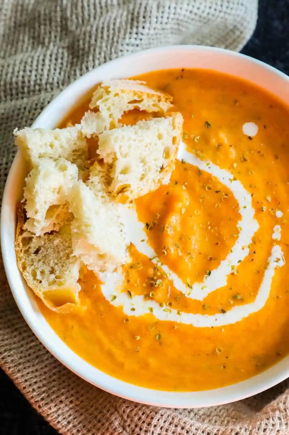 A bowl of carrot soup with croutons and sour cream.
