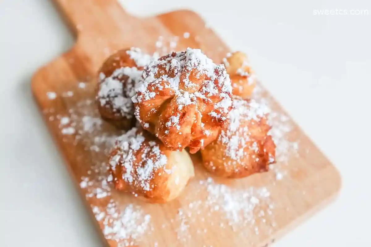 Powdered doughnuts with powdered sugar on a wooden cutting board, inspired by the 3 Ingredient Fried Peanut Butter Jelly Bomb recipe.