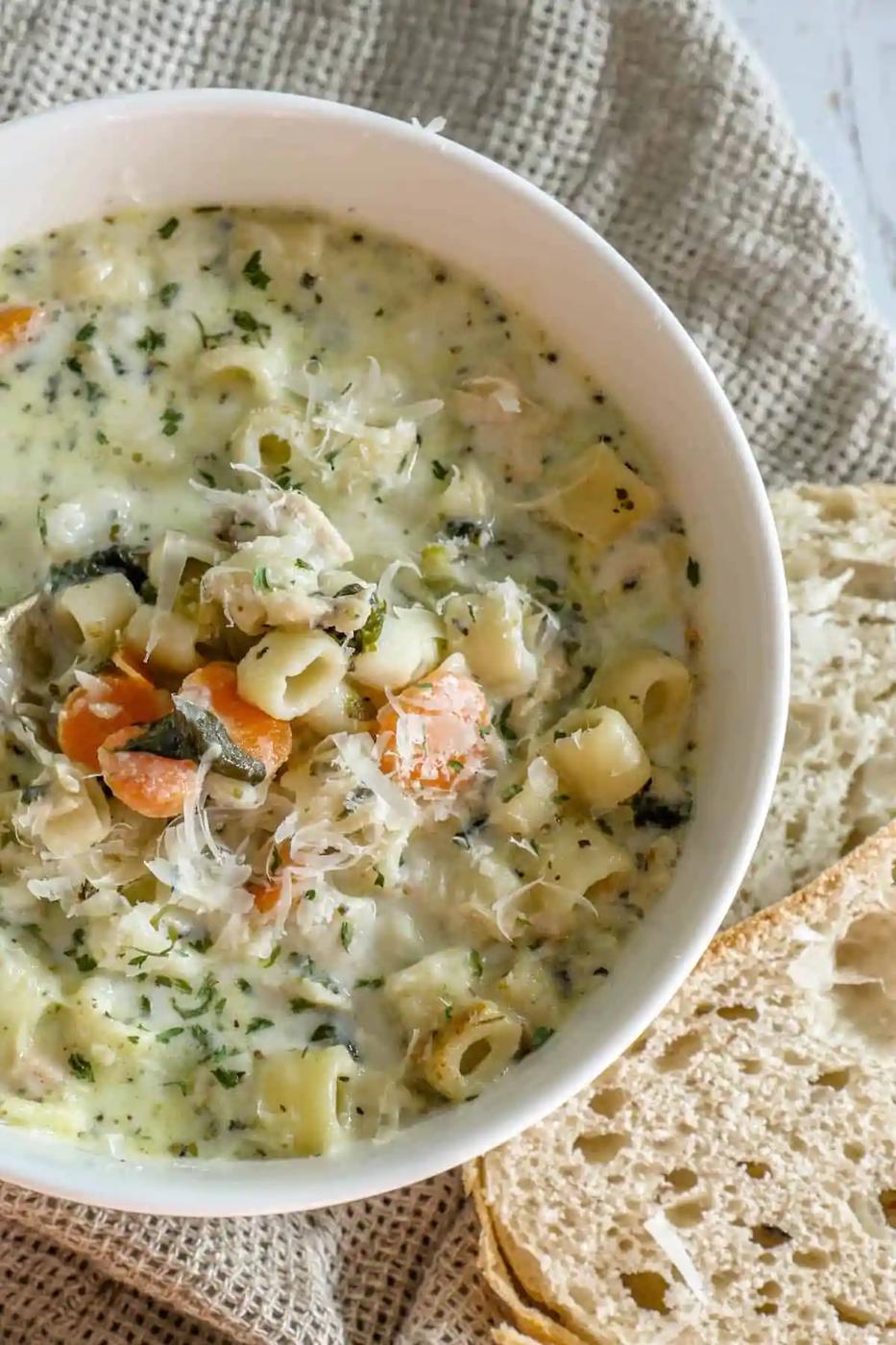 A creamy bowl of chicken noodle soup with bread next to it.