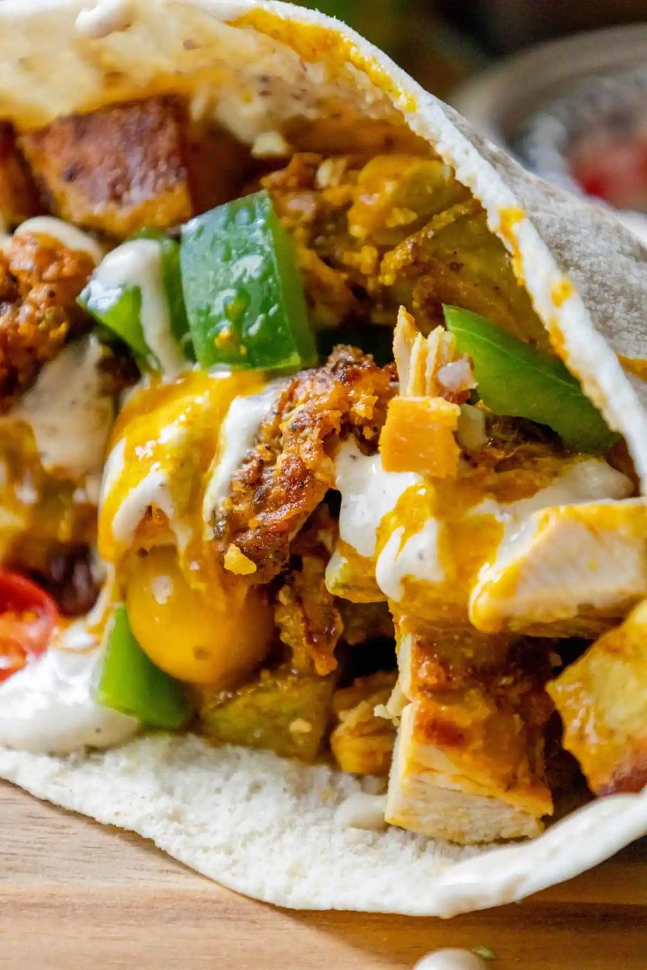 A chicken shawarma burrito on a wooden cutting board.