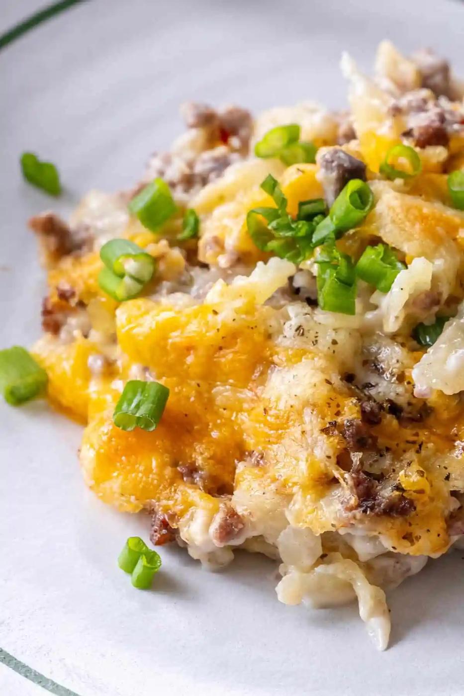 A serving of cheesy casserole with ground beef, topped with chopped green onions, on a white plate.