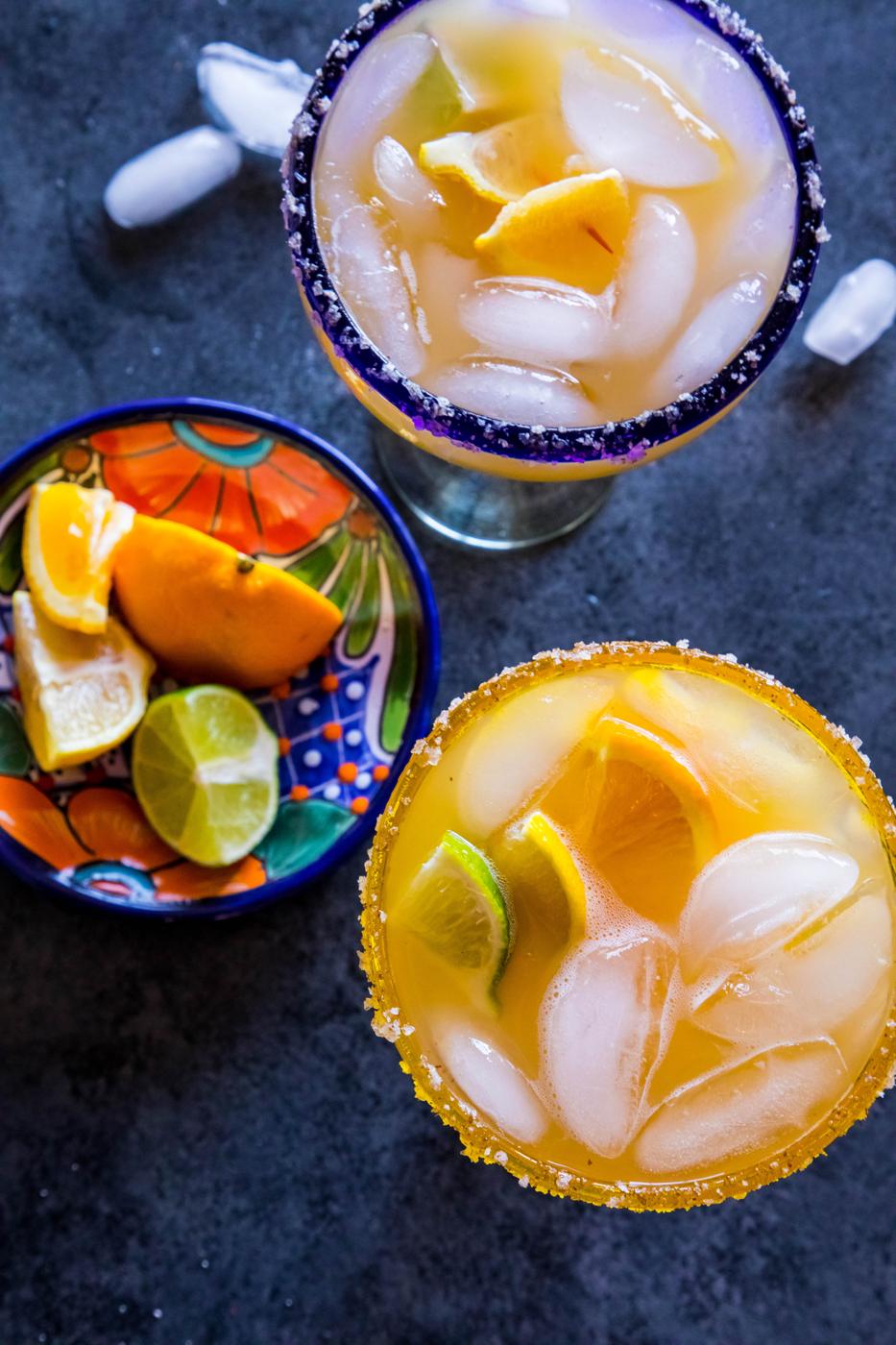 2 yellow margarita with lemon and lime wedges in it