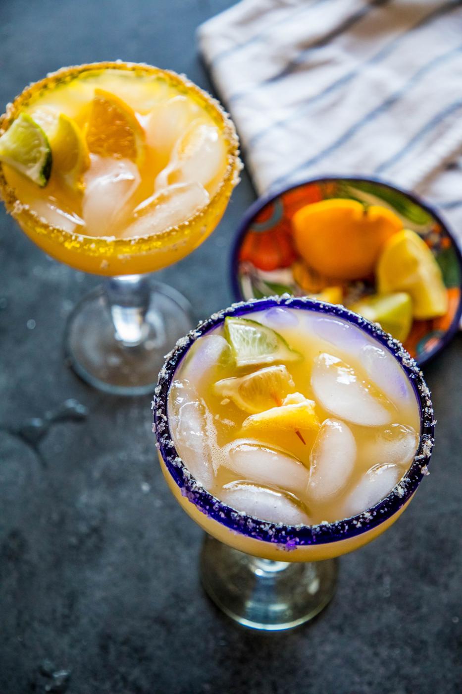 2 yellow margarita with lemon and lime wedges in it