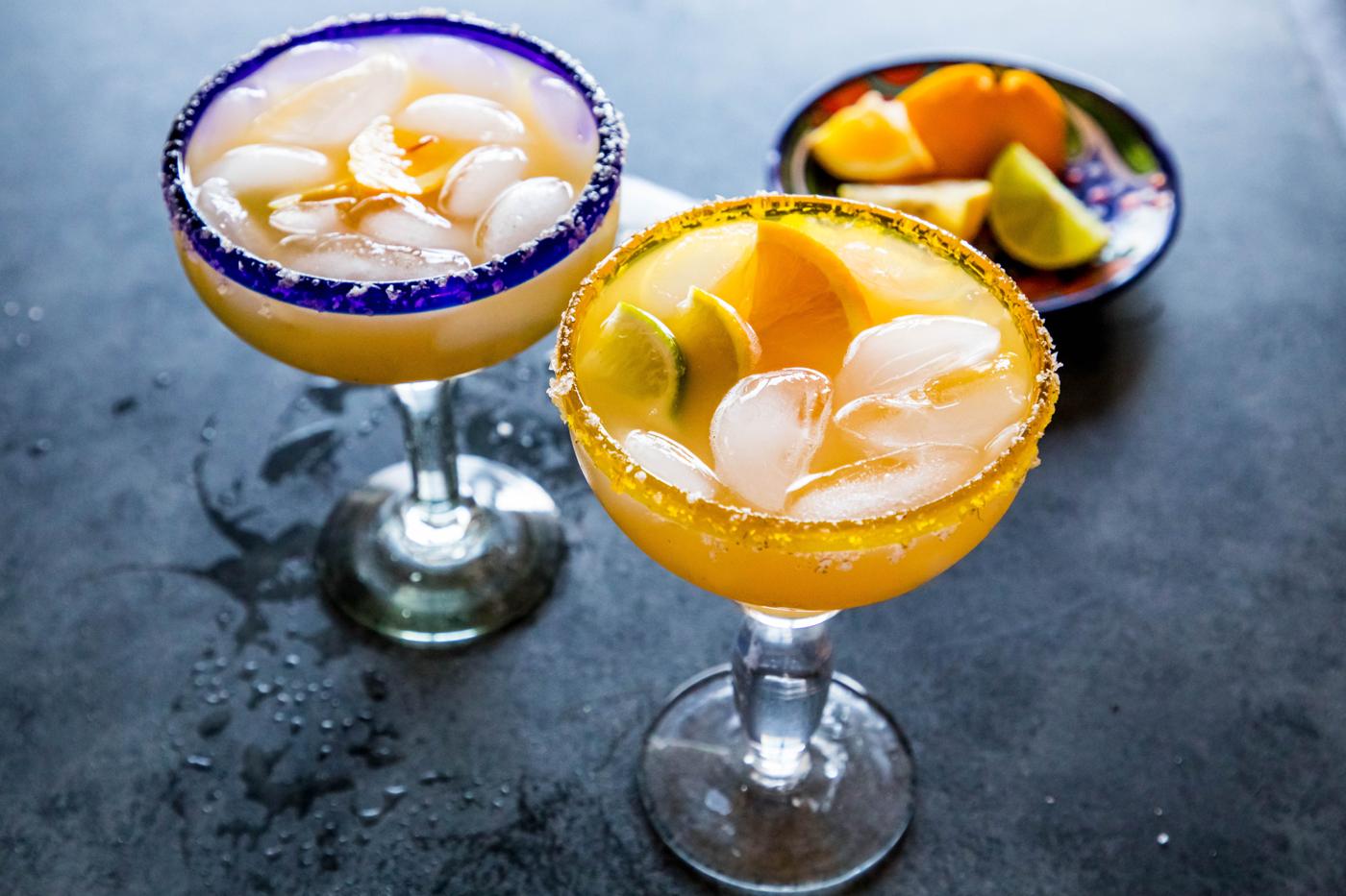 2 yellow margarita with lemon and lime wedges in it