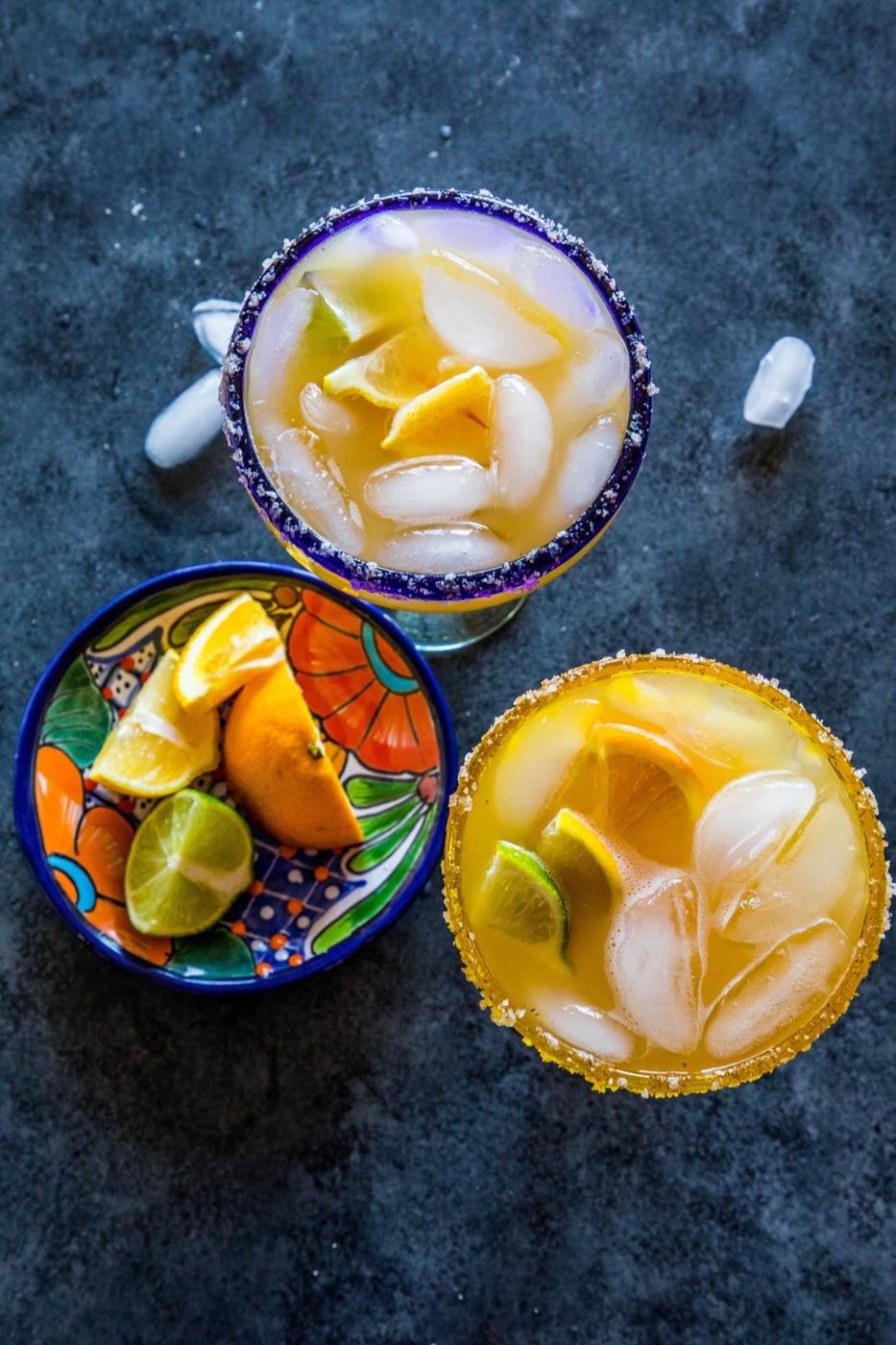 2 yellow margarita with lemon and lime wedges in it
