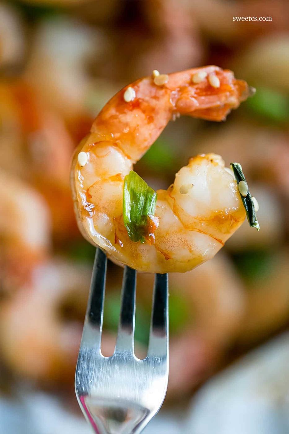 cooked shrimp with sesame seeds and green onions on them on a fork