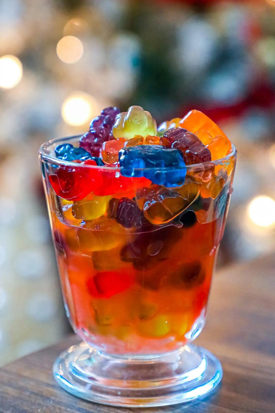 Boozy Negroni gummy bears in a glass with a Christmas tree in the background.