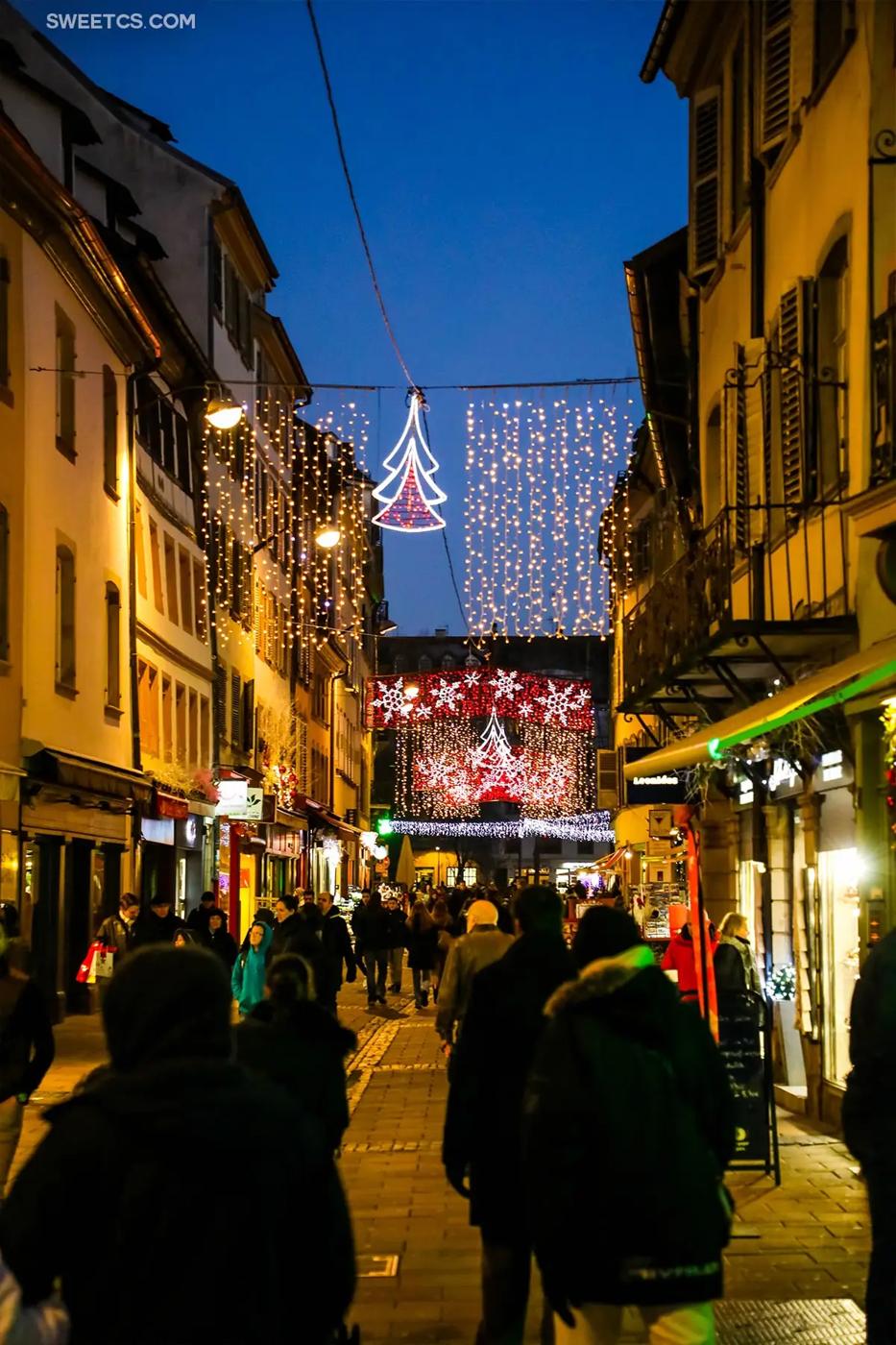 People walking down a street in Strasbourg, France surrounded by Christmas lights.