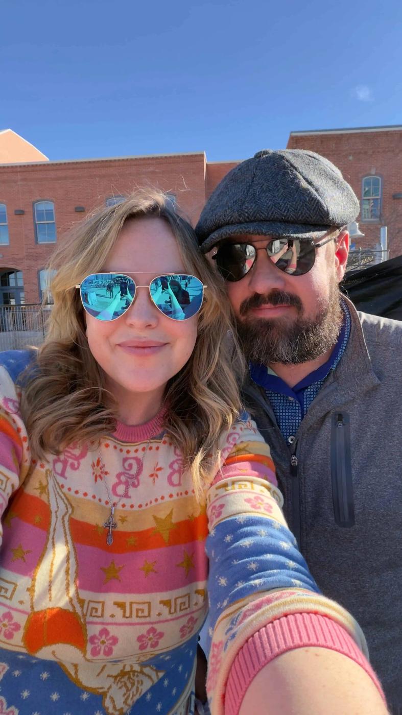 Two people wearing sunglasses pose for a selfie outdoors on a sunny day, with brick buildings in the background—capturing a fun moment for the Ajpal Blog.