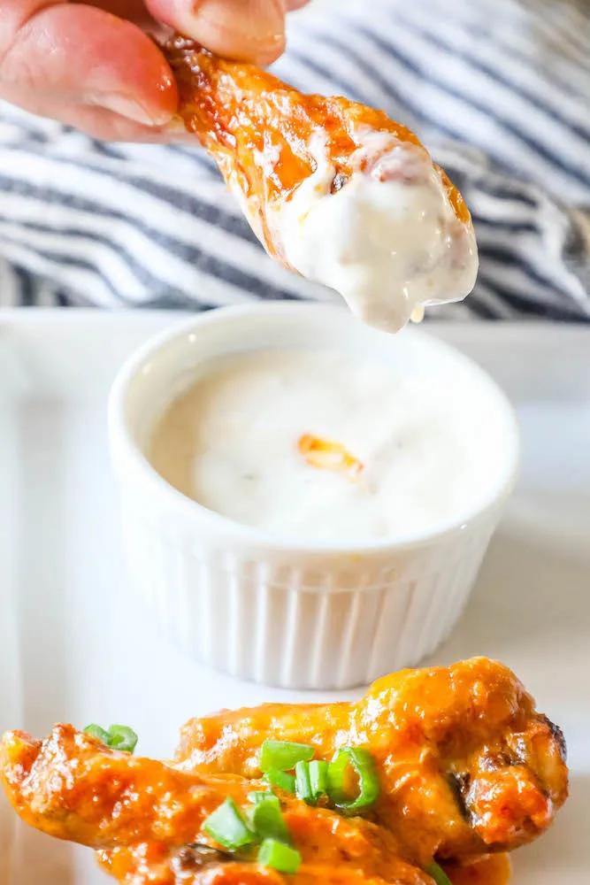 A person is air frying Nandos wings, dipping them into a sauce.