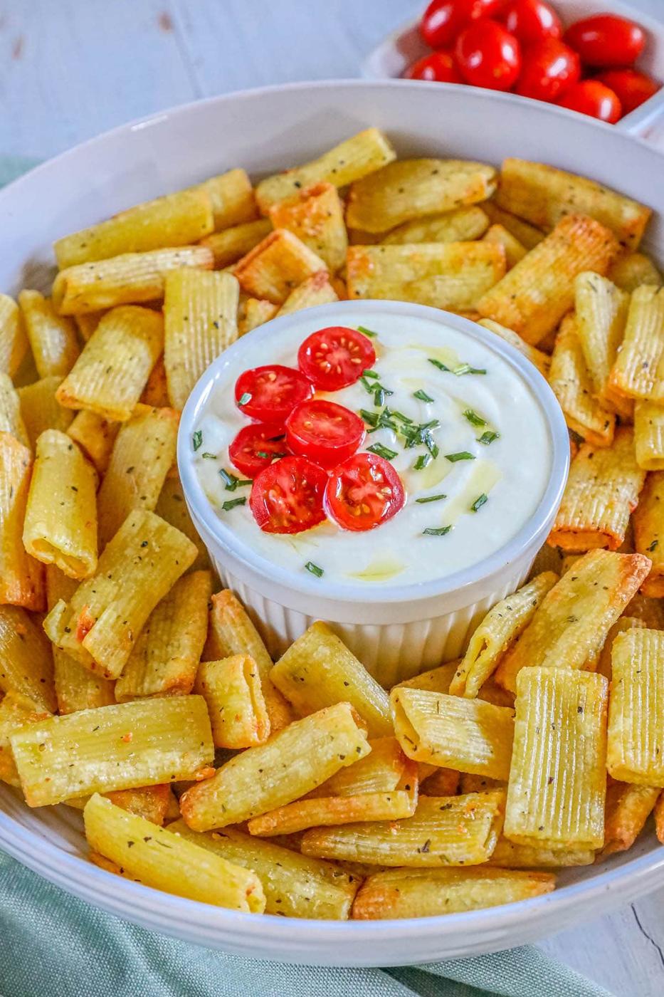 picture of air fried pasta chips in a bowl with feta dip with tomatoes sliced on top