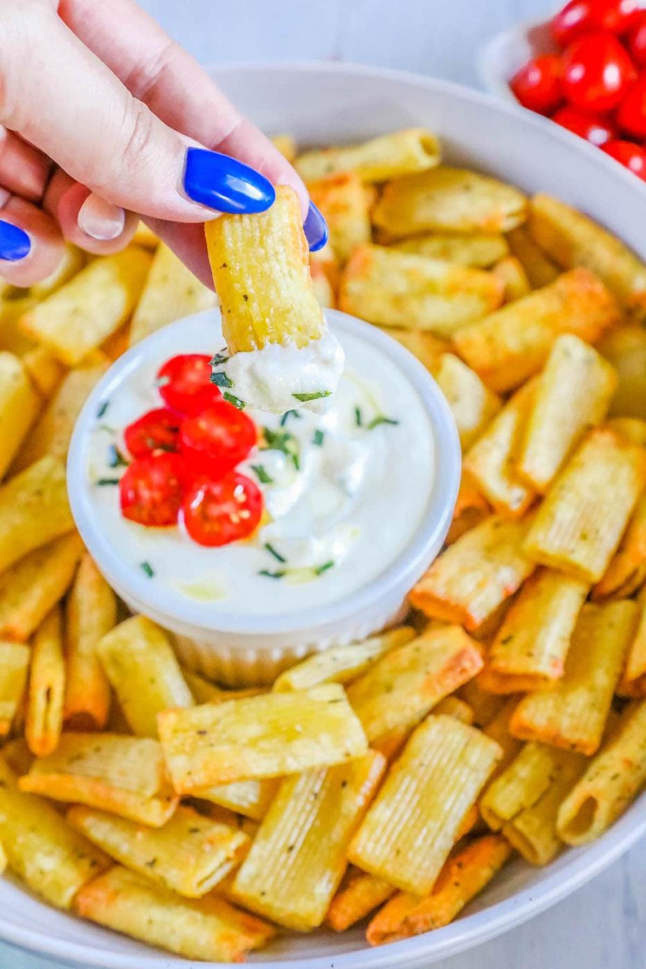 picture of air fried pasta chips in a bowl with feta dip with tomatoes sliced on top