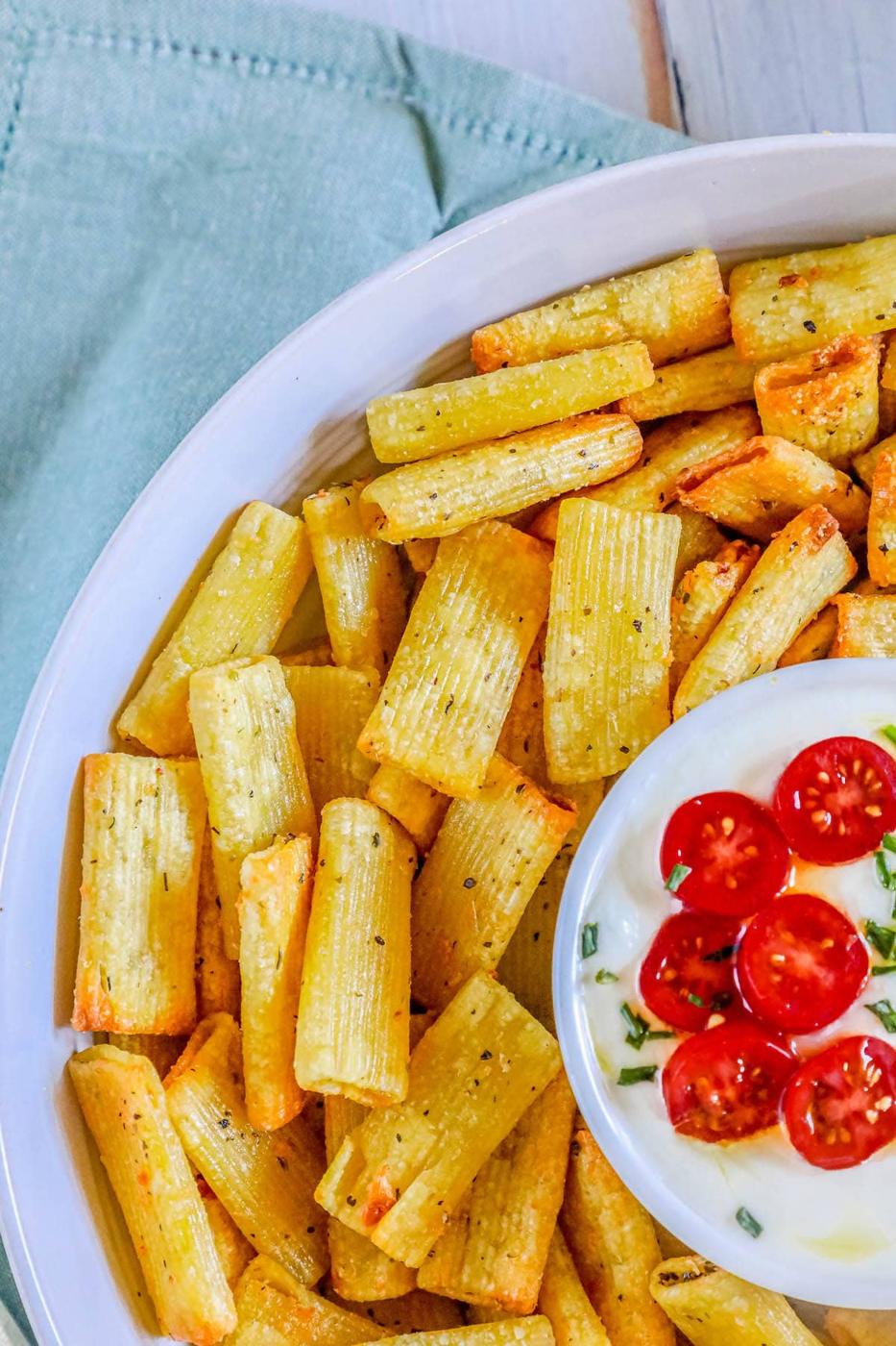 picture of air fried pasta chips in a bowl with feta dip with tomatoes sliced on top
