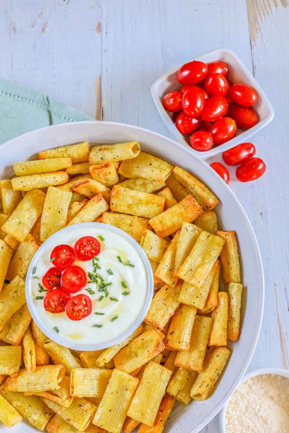 picture of air fried pasta chips in a bowl with feta dip with tomatoes sliced on top