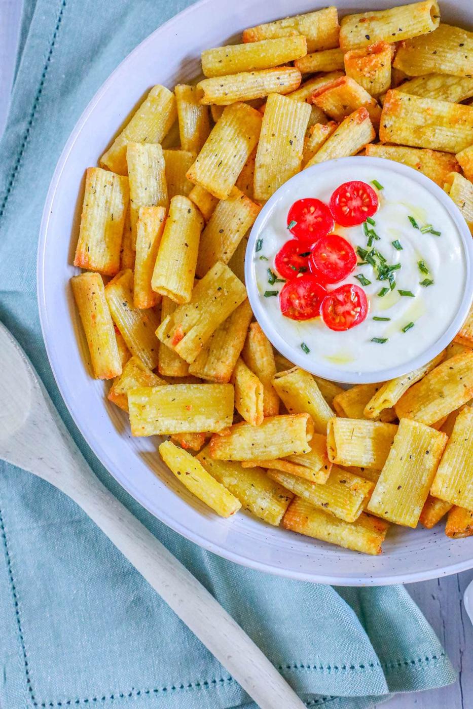 picture of air fried pasta chips in a bowl with feta dip with tomatoes sliced on top