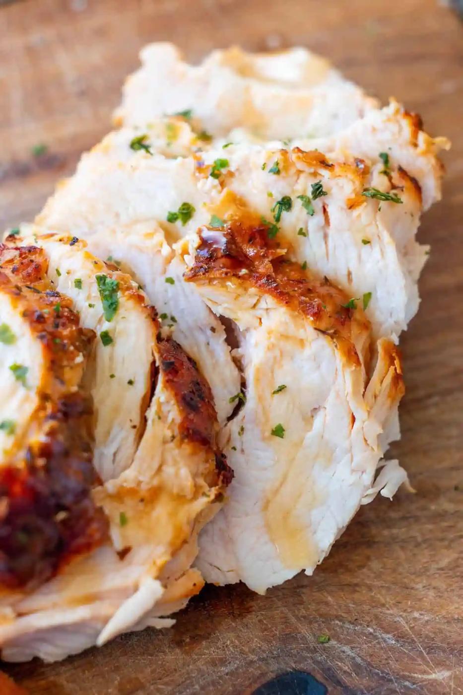 Sliced cooked turkey breast garnished with chopped herbs on a wooden cutting board.