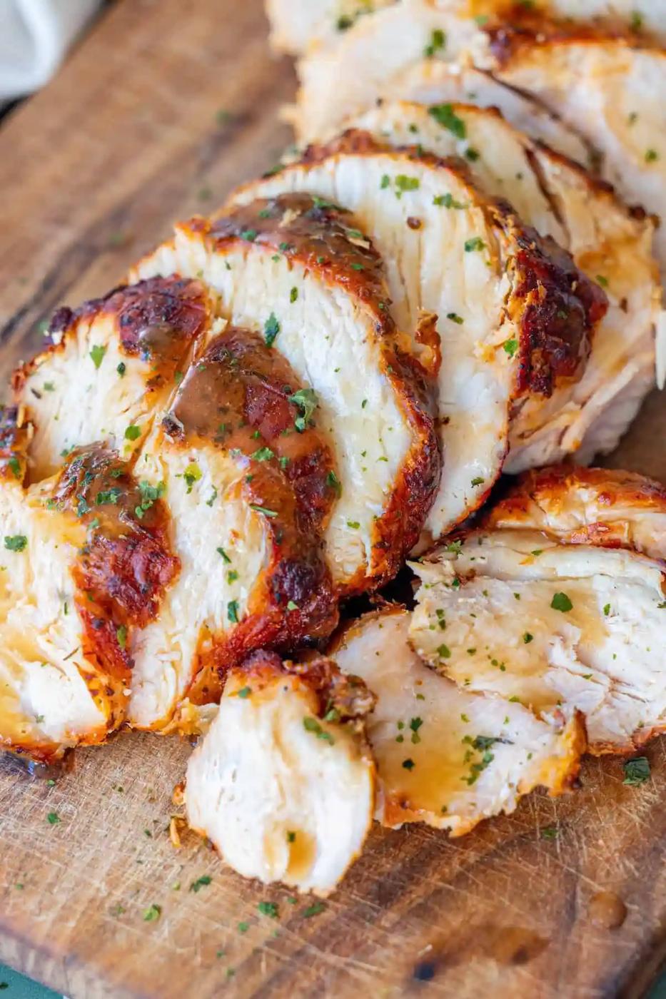 Sliced, cooked chicken breast with a golden, seasoned crust and garnished with chopped herbs on a wooden cutting board.