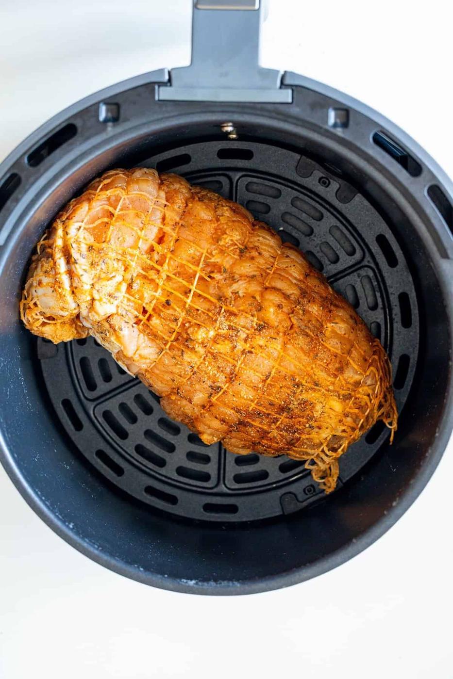 A seasoned, netted Cajun Turkey Breast sits inside the basket of an air fryer, ready for cooking.