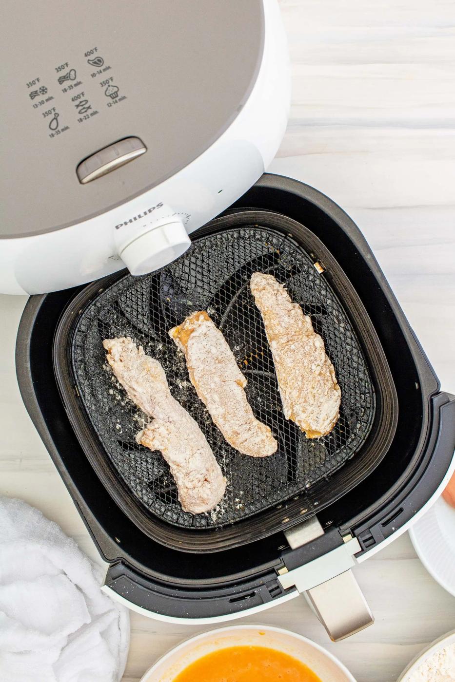 An air fryer with chicken tenders and vegetables inside.