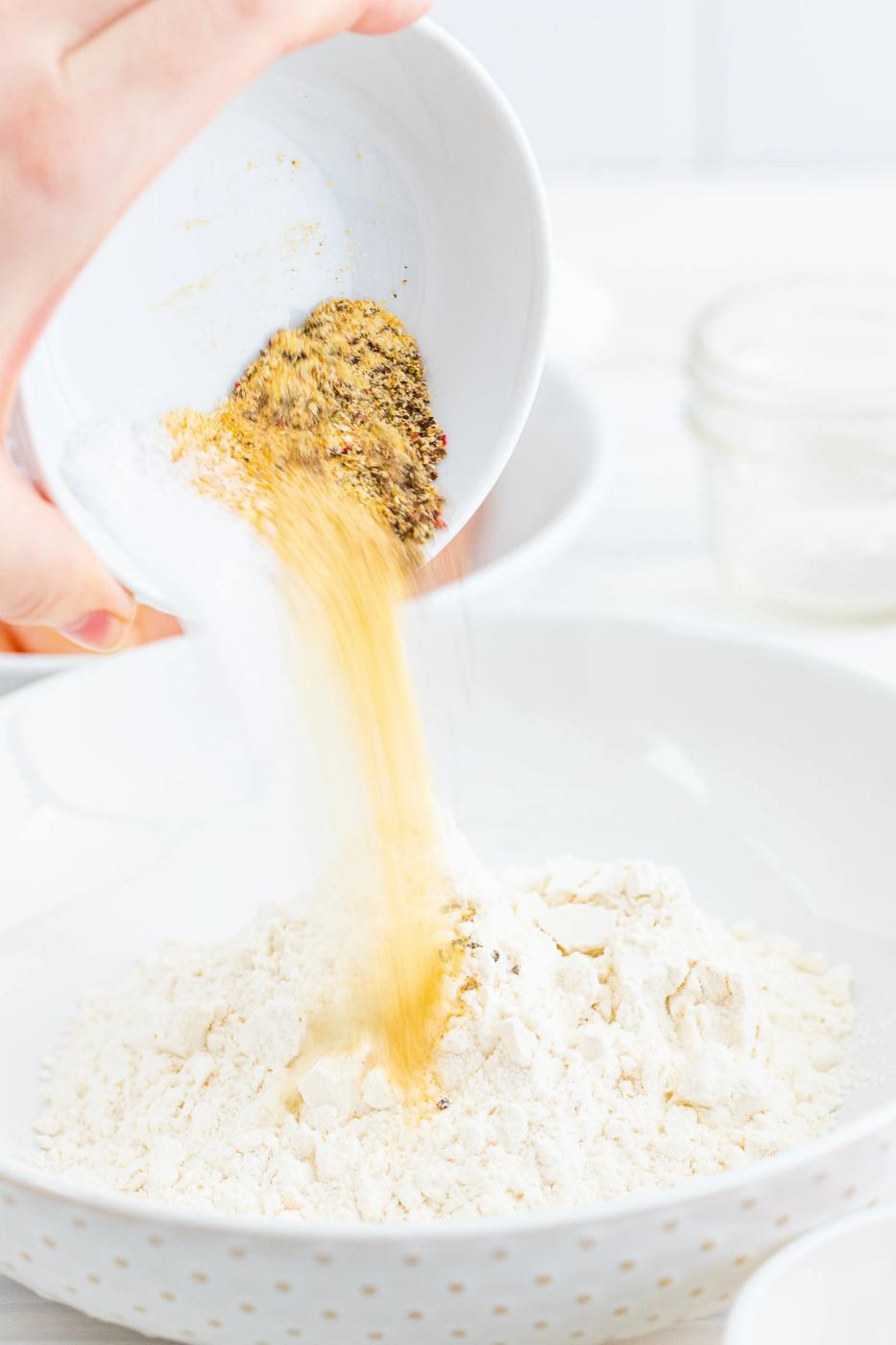 A person preparing chicken tenders by pouring flour into a bowl.