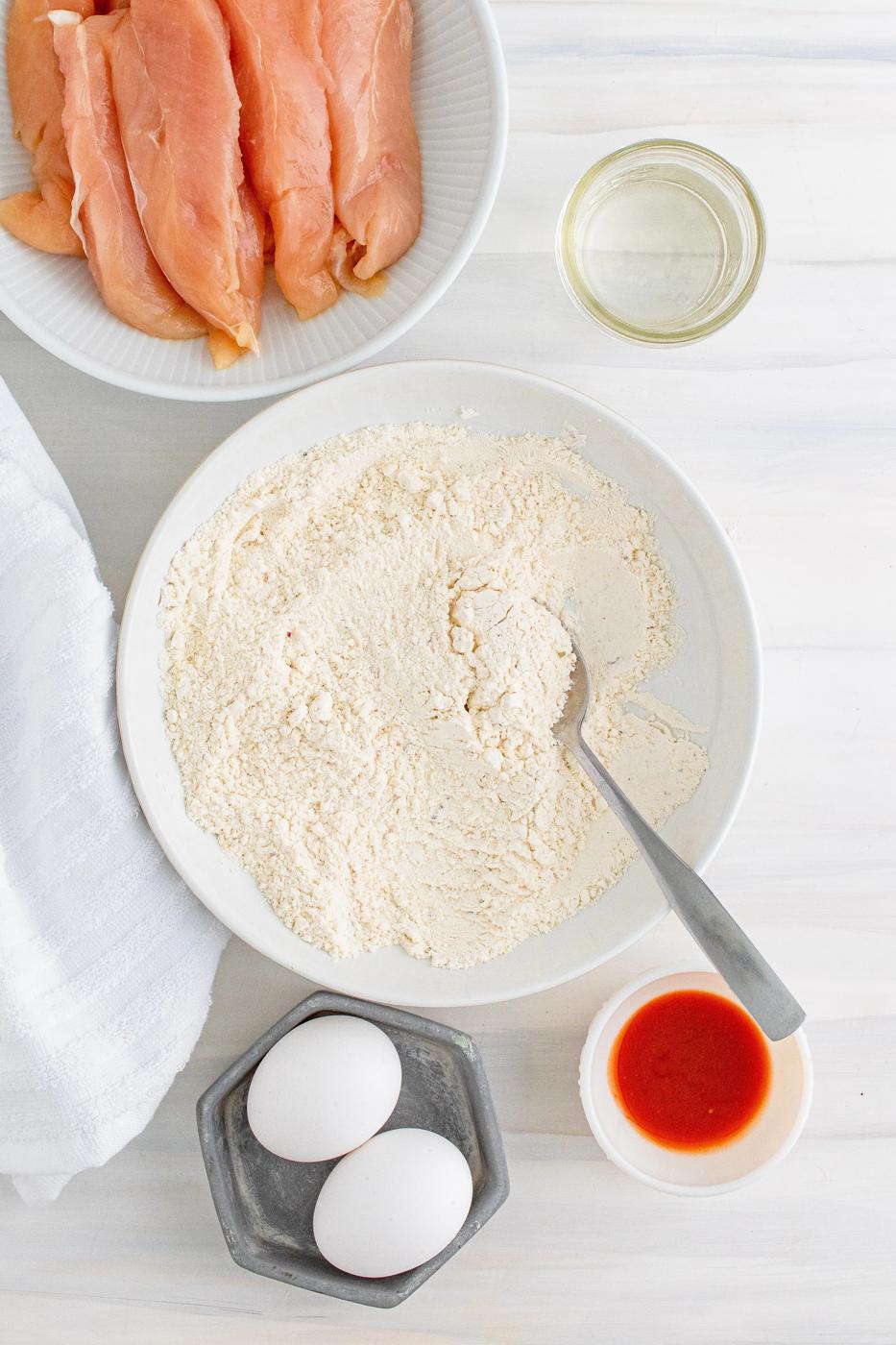 A bowl of chicken fingers ingredients on a white table.