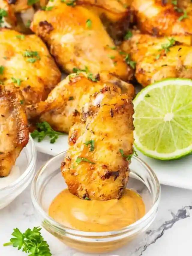 A plate of chicken wings with sauce and lime wedges.