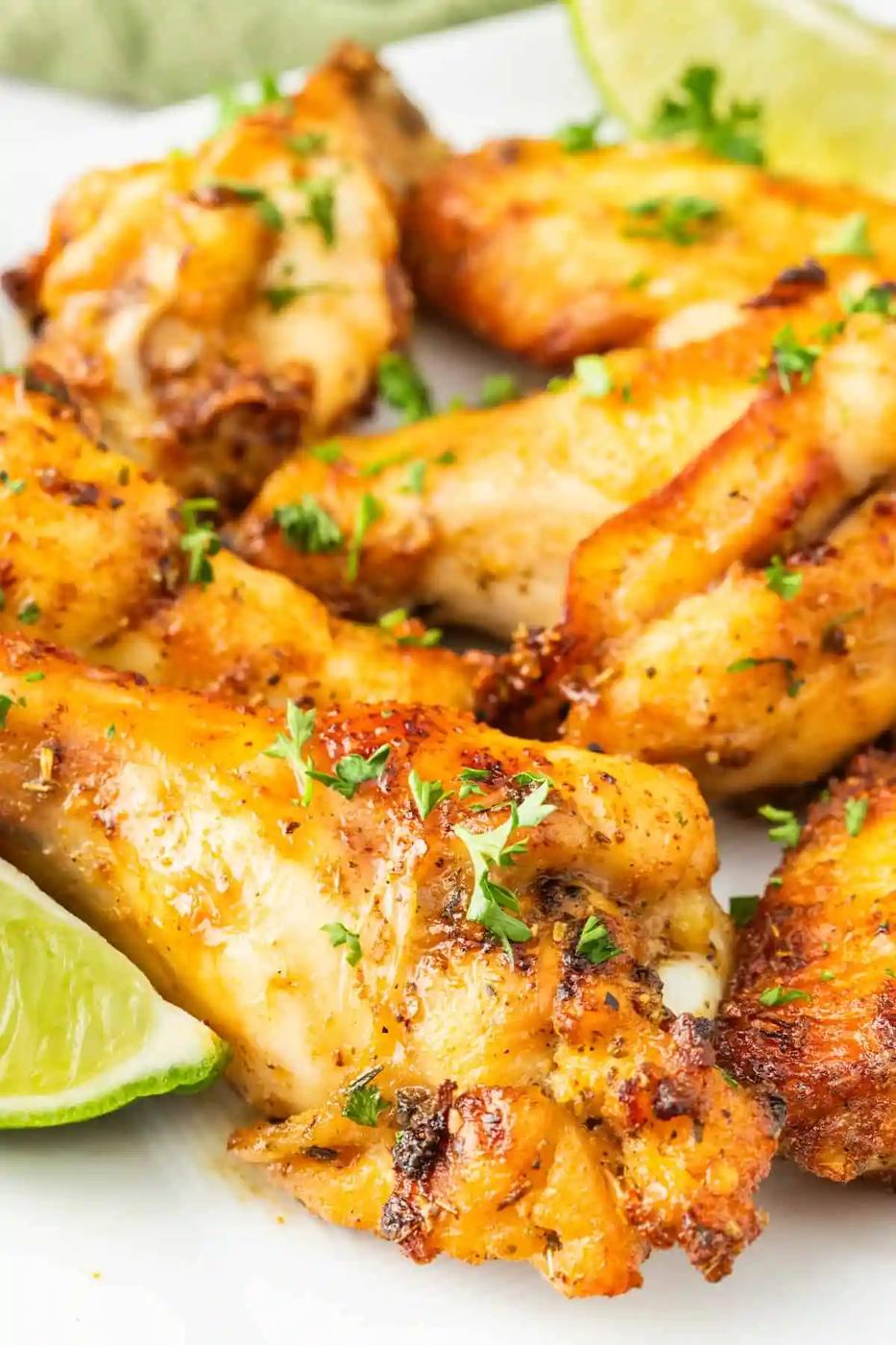Air-fried chicken wings on a white plate with lime wedges.