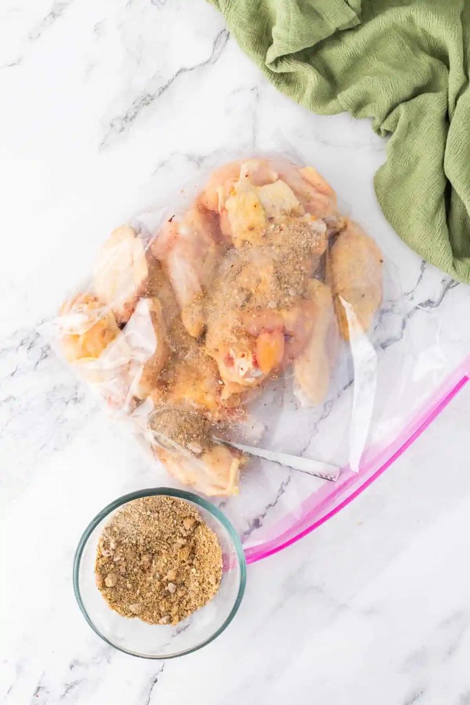 A bag of chicken wings in a plastic bag next to a spoon.