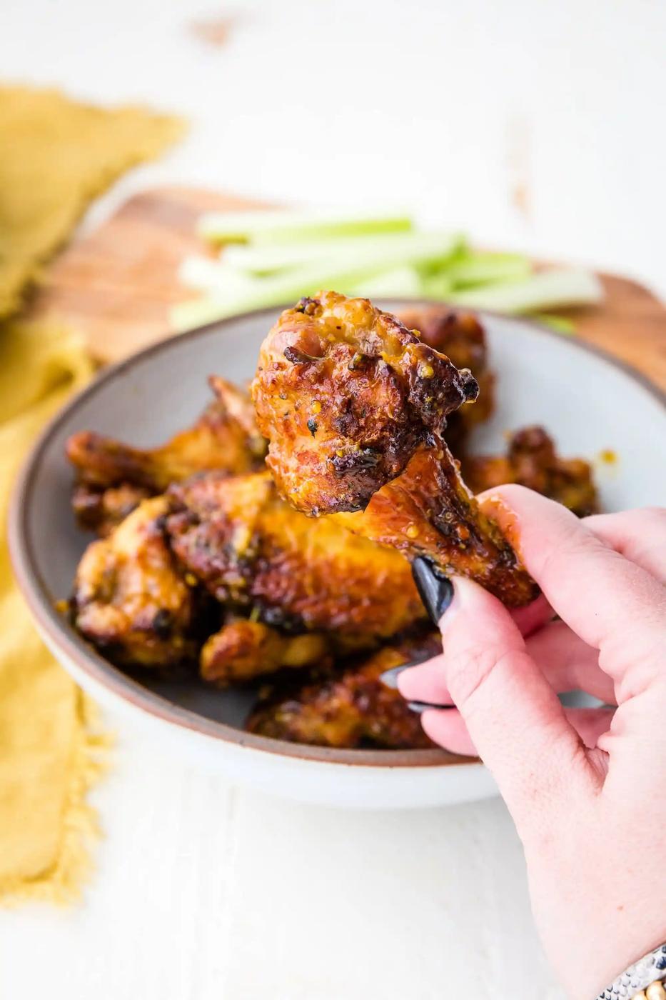 A hand is holding a bowl of honey mustard chicken wings.