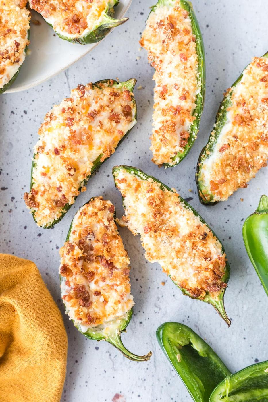 air fried jalapeño peppers sliced in half stuffed with cream cheese mixture and bread crumbs on a speckled plate next to a yellow towel