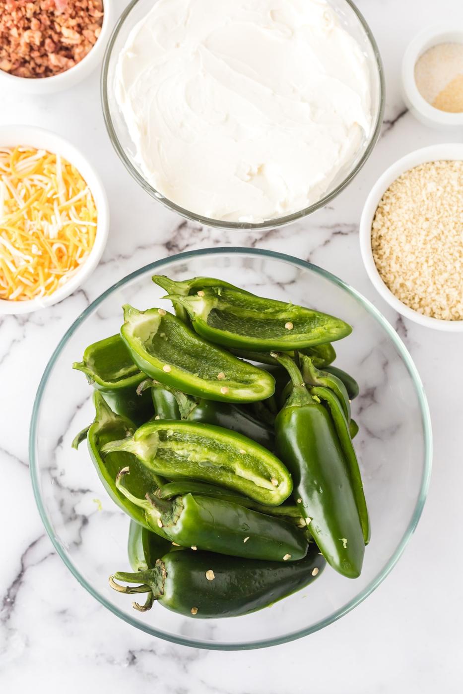 jalapeno peppers cut in half in a bowl on a table next to bowls of cheese