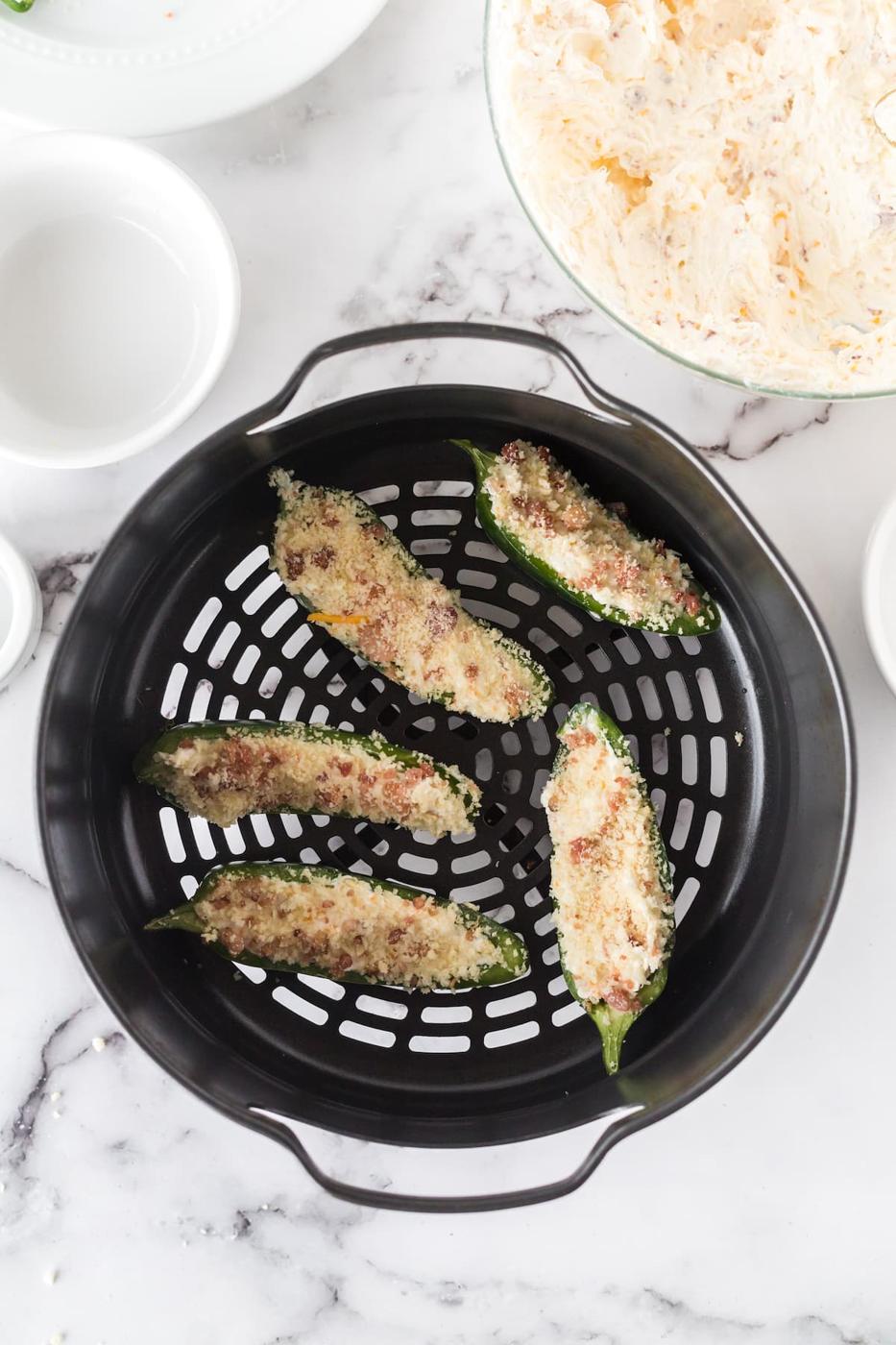 jalapeño pepper cut in half filled with cream cheese filling and topped with panko breadcrumbs in the basket of an air fryer