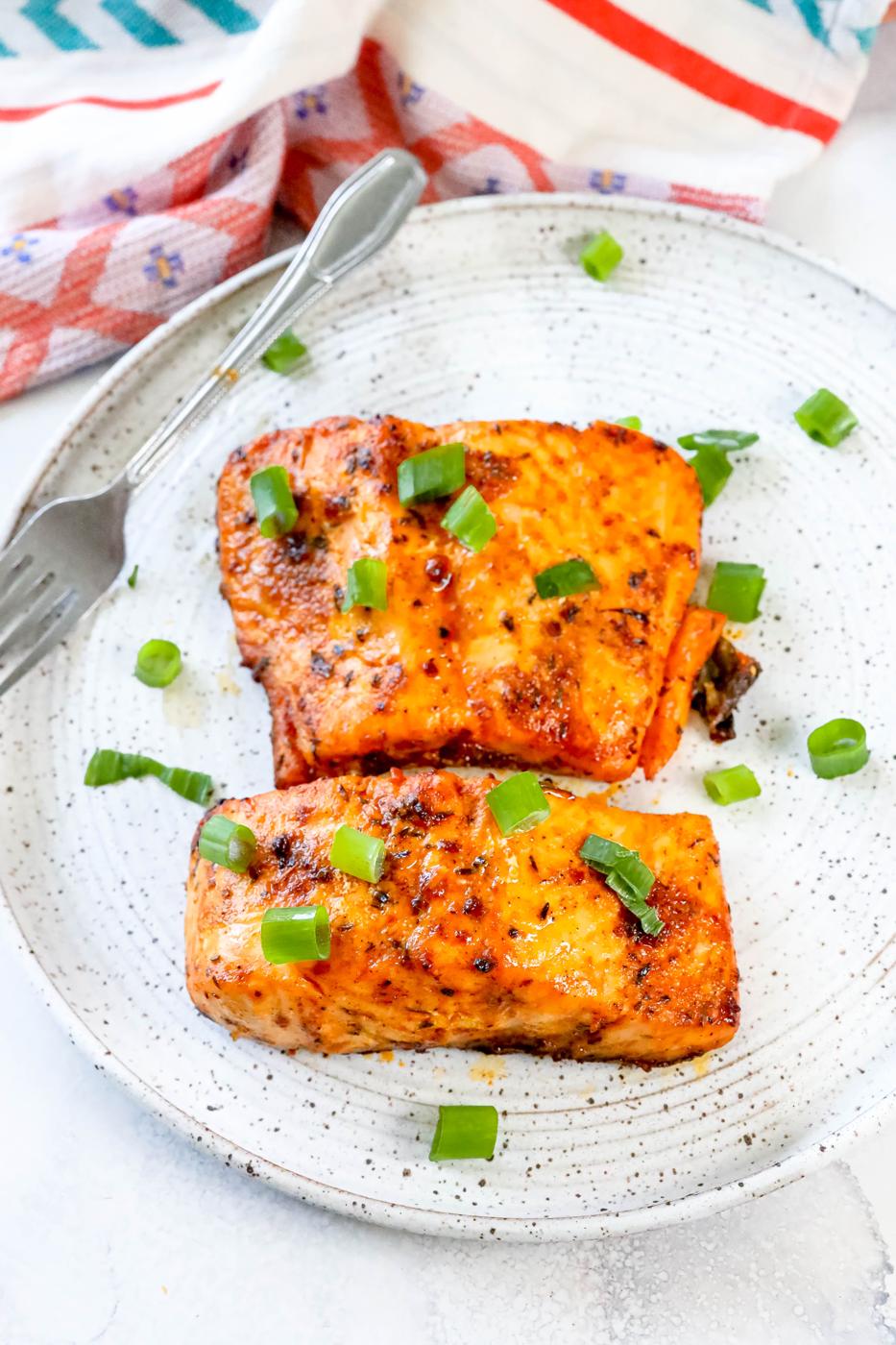 salmon with spices cooked on a white plate with green onions on it