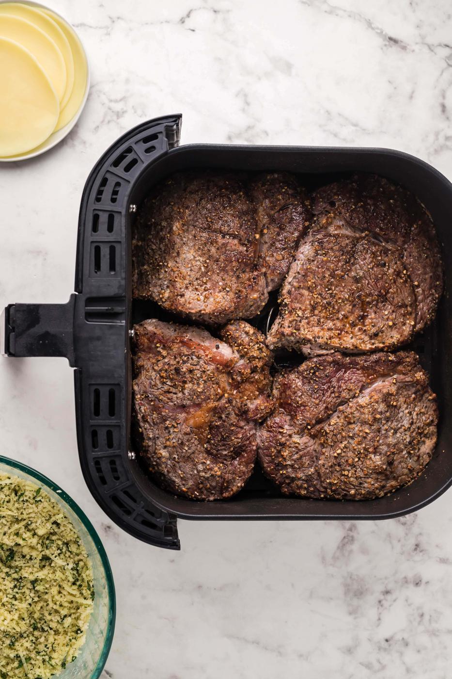 A pan with parmesan crusted steak next to a bowl of spices.