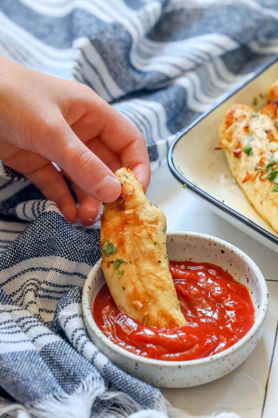 a hand dipping a naked chicken tender into ketchup