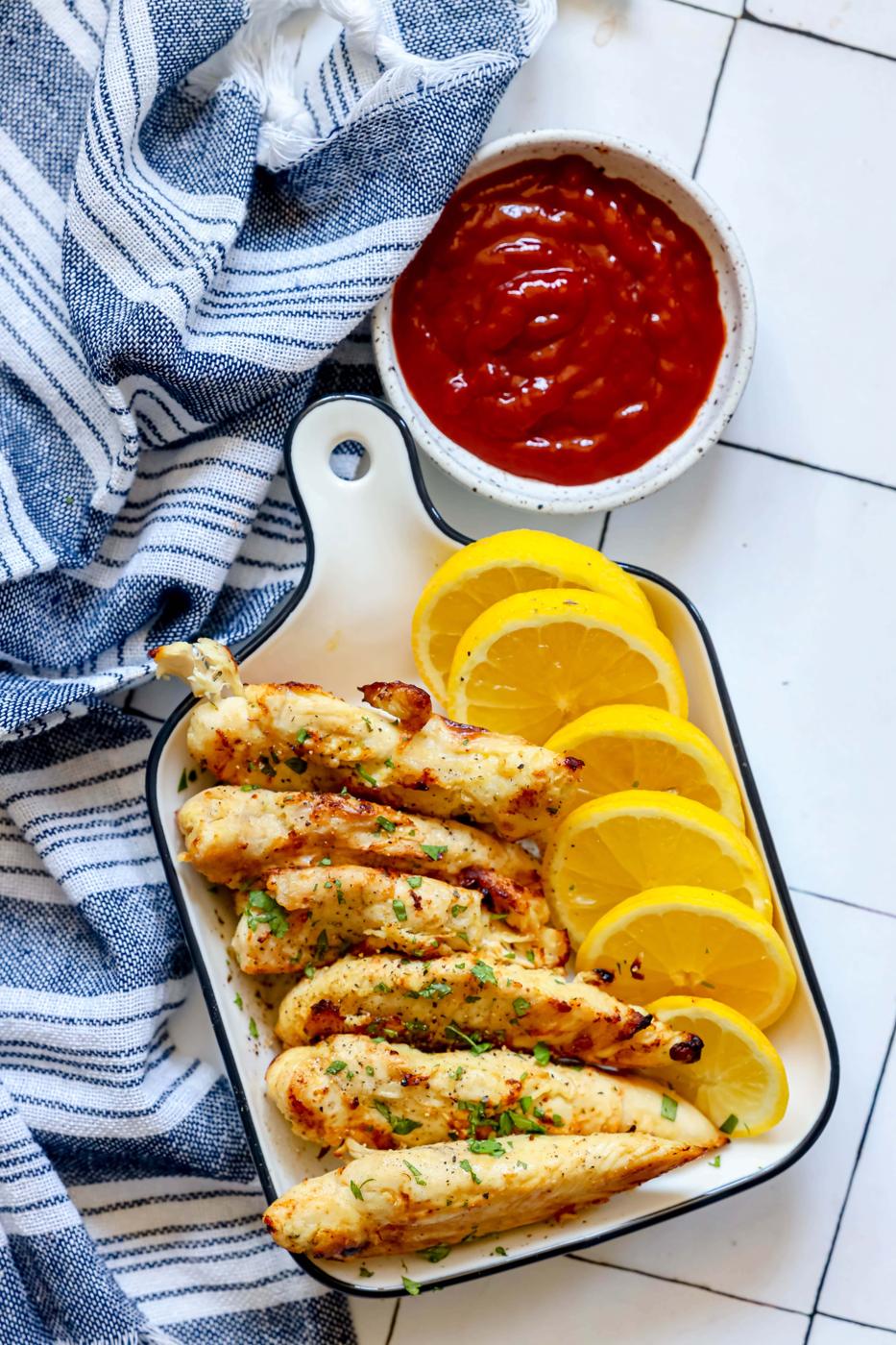 naked chicken tenders in a white dish with lemon slices next to them