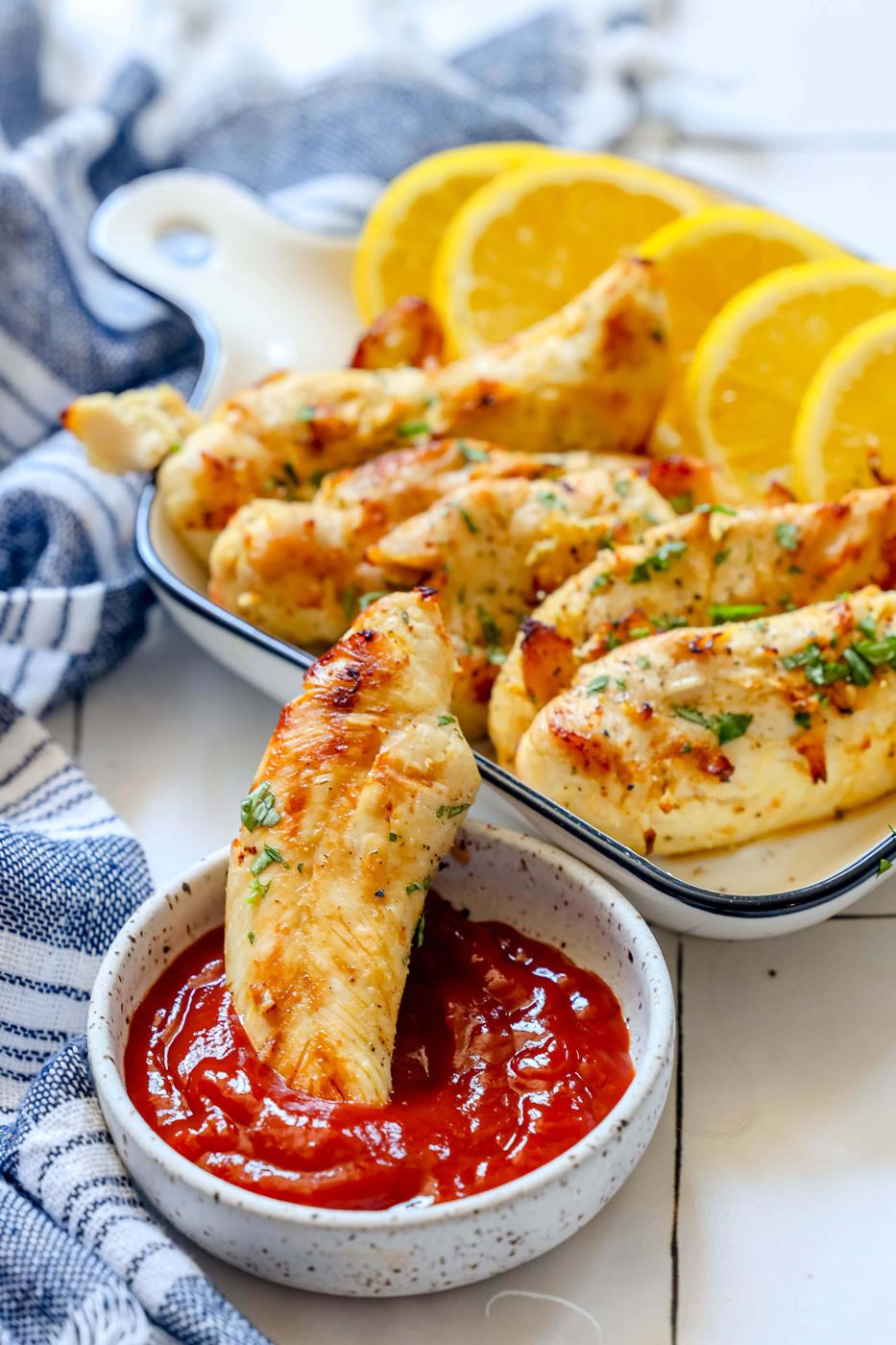 air fried chicken tender being dipped in a bowl of ketchup