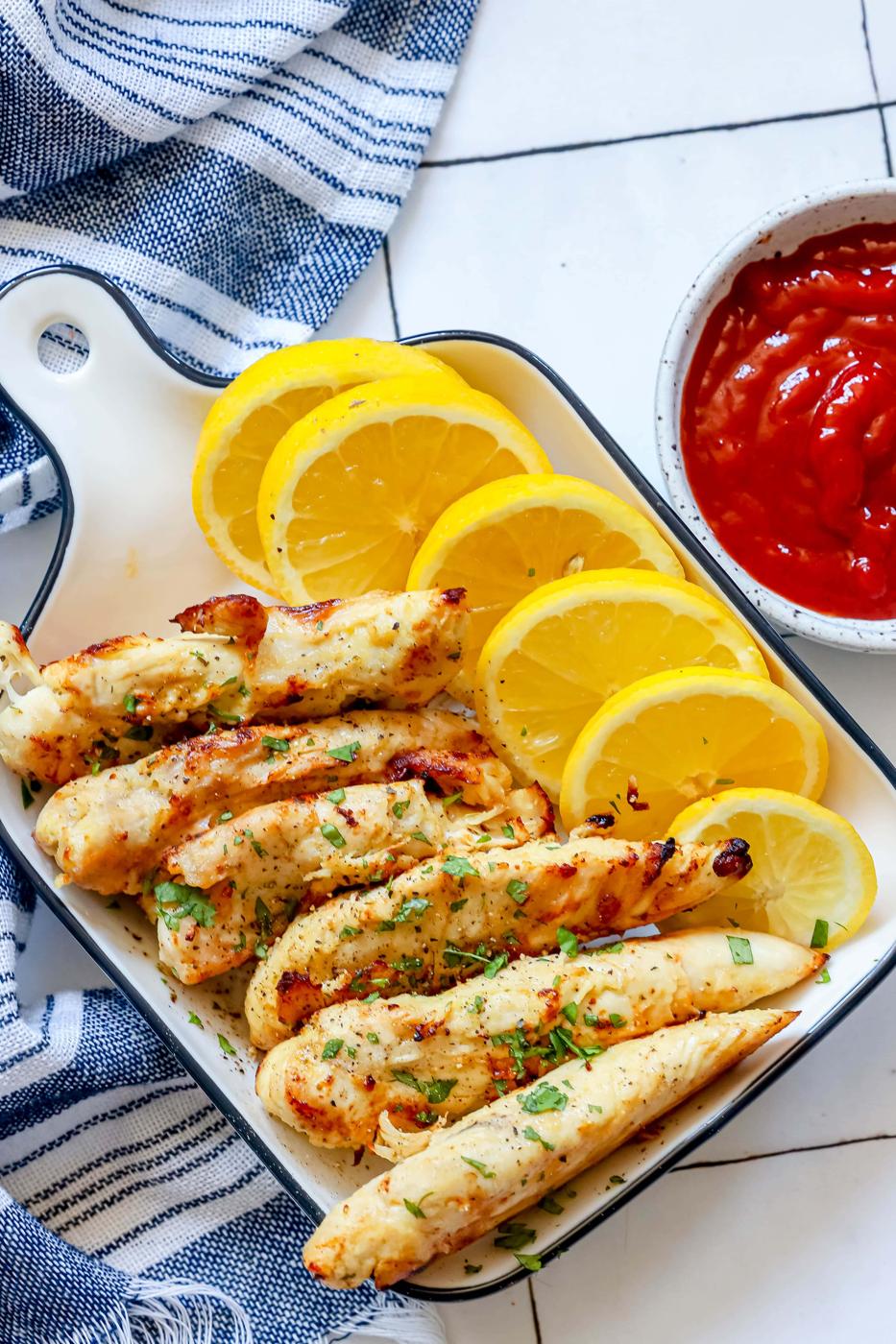 unbreaded chicken tenders in a white dish with lemon slices next to them