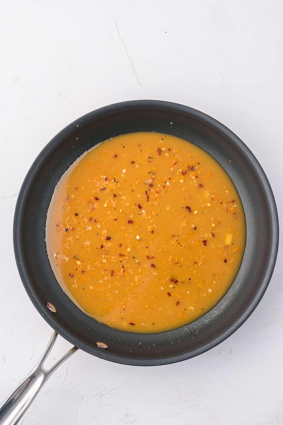 An Air Fryer frying pan with Orange Chicken sauce sizzling inside.