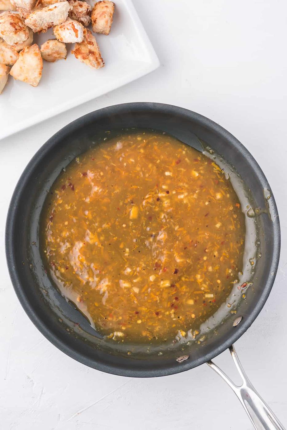 An air fryer frying pan with orange chicken sauce on it.