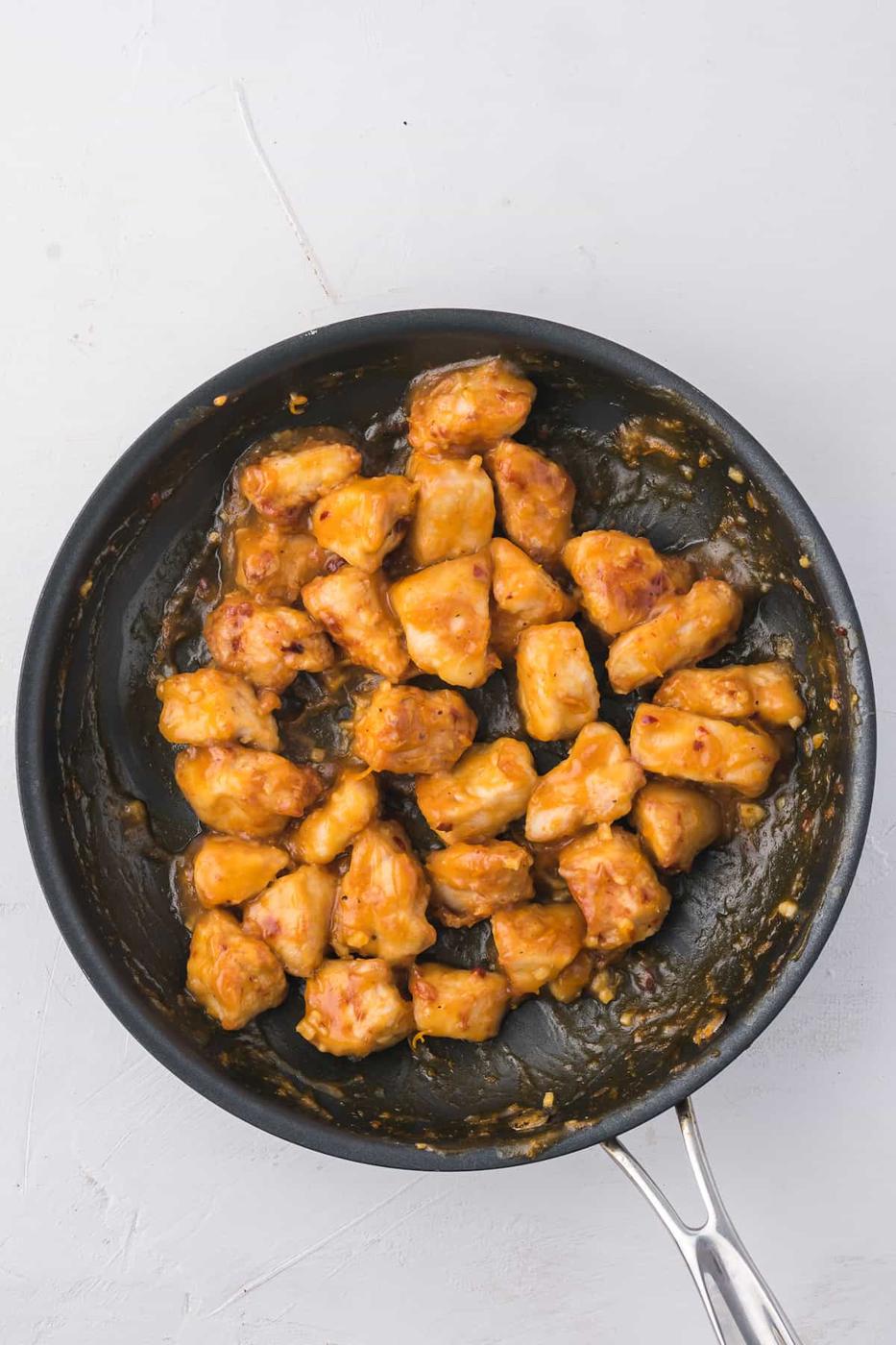 Orange chicken in an air fryer on a white background.