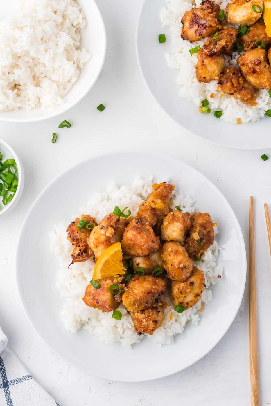 A white plate with orange chicken and rice on it.