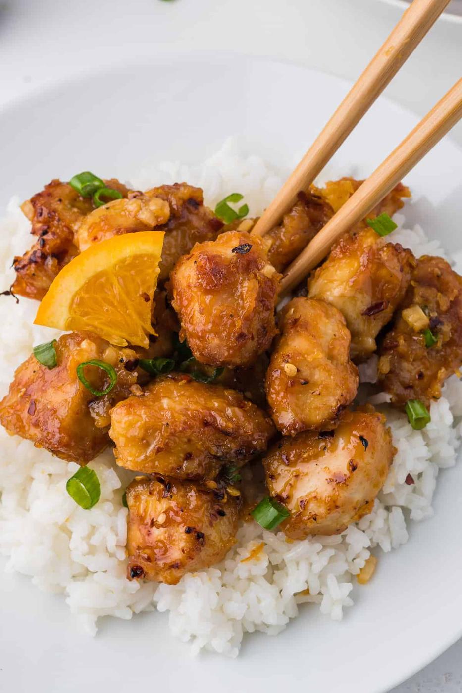 A white plate with Orange Chicken and oranges on it.
