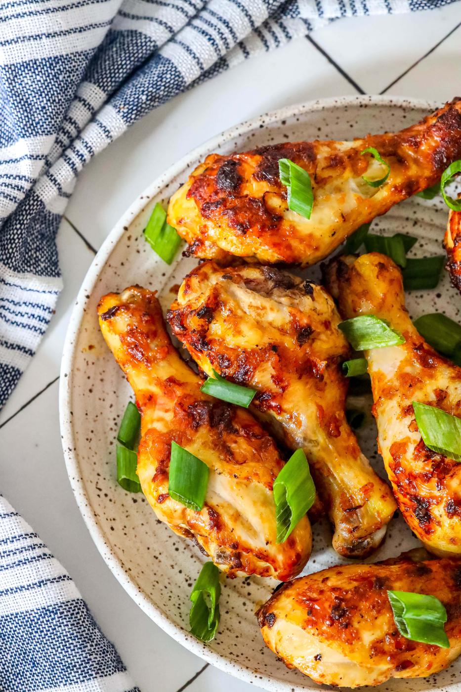 picture of spiced chicken drumsticks with green onions on a white plate with blue towel in the background.